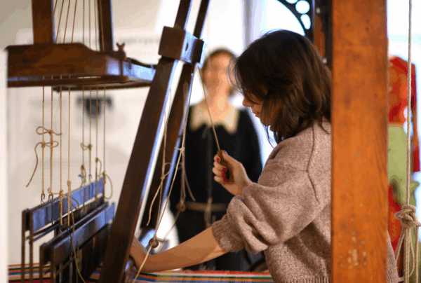 Guide en démonstration sur un métier à tisser traditionnel, montrant la technique de fabrication des tissus de soie au musée Brochier Soieries